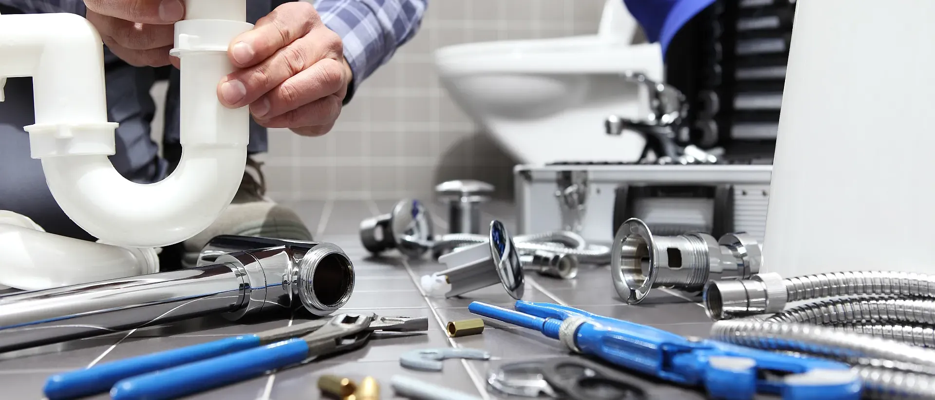 Klempner setzt ein Siphon unter dem Waschbecken zusammen, Werkzeuge am Boden.